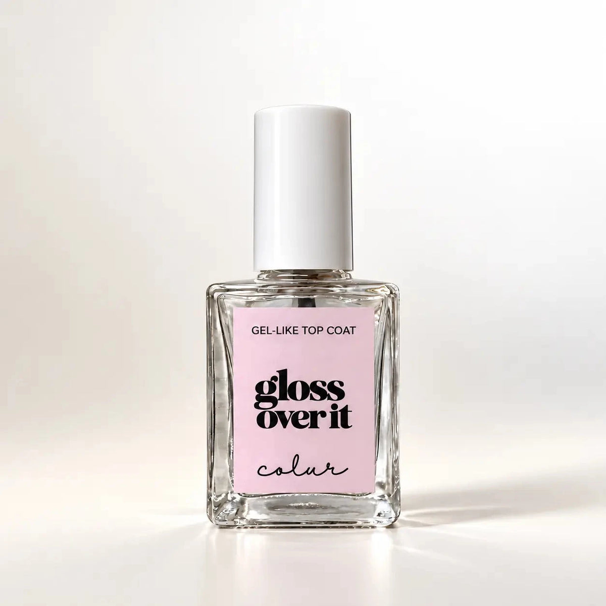 A bottle of gloss over it color gel-like top coat nail polish on a clean white background. The bottle is clear glass with a white cap and a light pink label featuring black text.